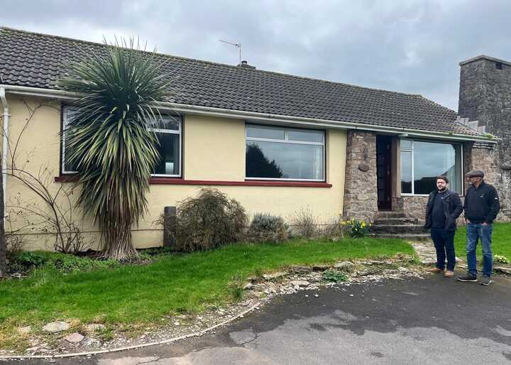 A single-story house with a garden, featuring two people standing outside.