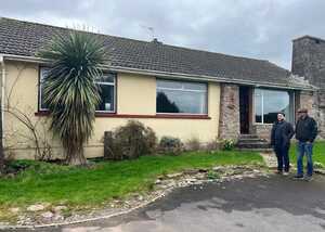 A single-story house with a garden, featuring two people standing outside.