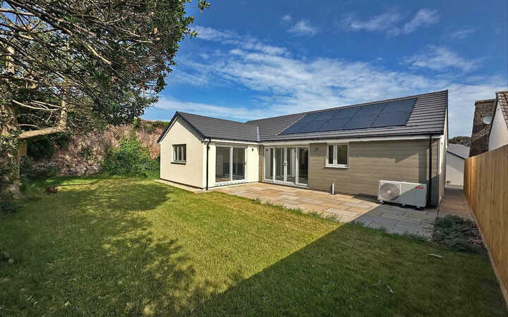 Modern house with a garden under a blue sky, featuring solar panels on the roof.
