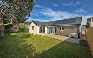 Modern house with a garden under a blue sky, featuring solar panels on the roof.