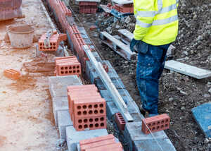 Worker in a yellow safety jacket stands near brickwork on a construction site.