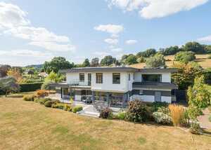 Modern two-story house surrounded by a landscaped garden and rolling hills under a blue sky.