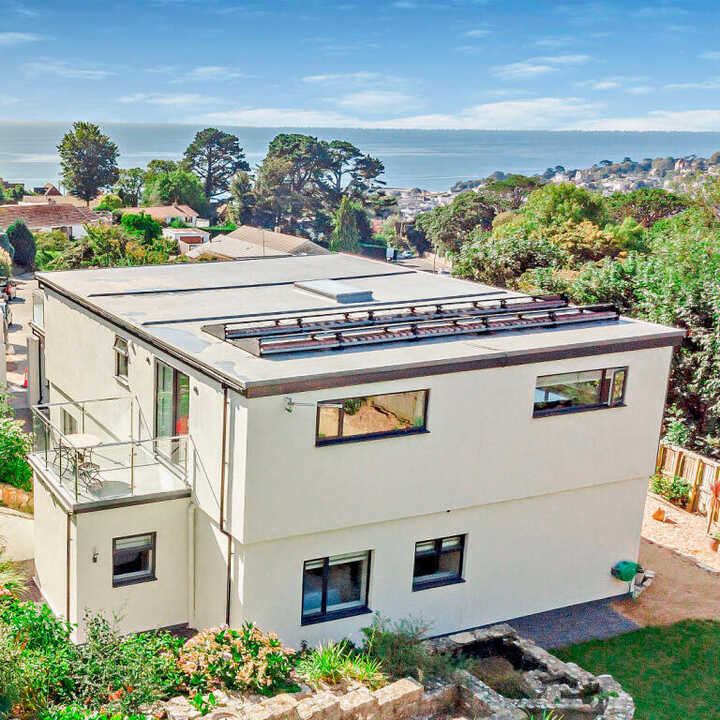 Modern two-story home with a rooftop and ocean view, surrounded by greenery.