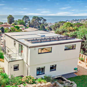 Modern two-story home with a rooftop and ocean view, surrounded by greenery.