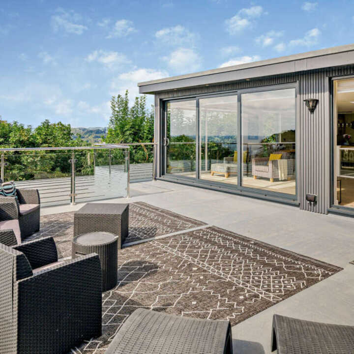 Modern outdoor seating area with a rug and large windows overlooking greenery.
