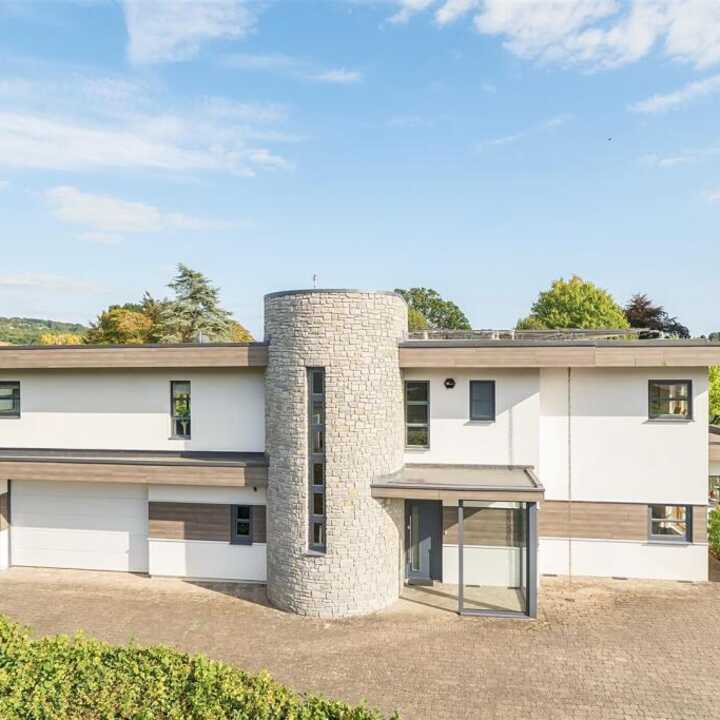 Modern two-story house with a cylindrical entrance and landscaped surroundings.