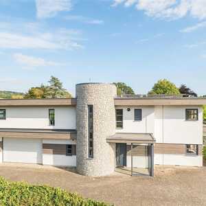 Modern two-story house with a cylindrical entrance and landscaped surroundings.