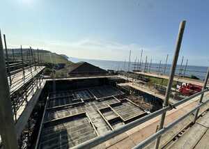 Construction site overlooking the sea with scaffolding and unfinished structures.