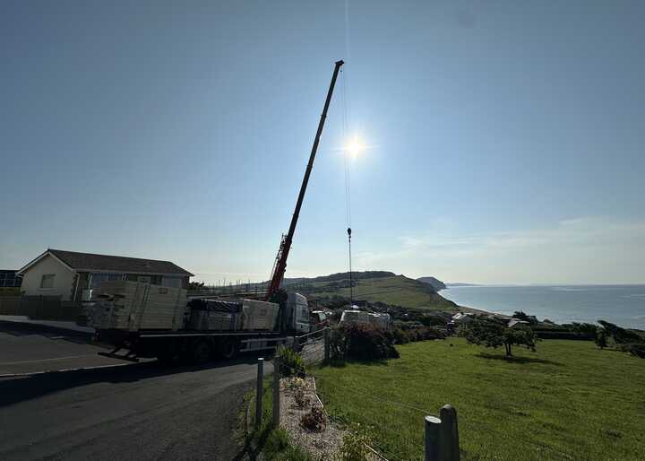 A crane on a truck beside a grassy area and ocean under a bright sun.