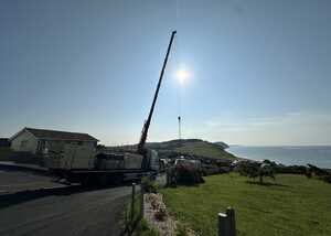 A crane on a truck beside a grassy area and ocean under a bright sun.