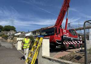 Construction scene with a red crane, workers in safety vests, and a ladder.