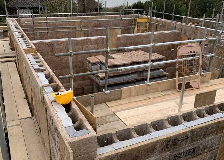 Construction site with a foundation, scaffolding, and wooden beams in a cloudy setting.