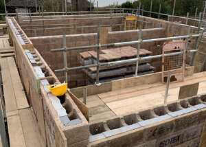 Construction site with a foundation, scaffolding, and wooden beams in a cloudy setting.