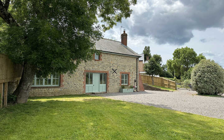 Stone cottage surrounded by grass and trees under a cloudy sky.