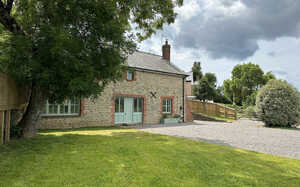 Stone cottage surrounded by grass and trees under a cloudy sky.