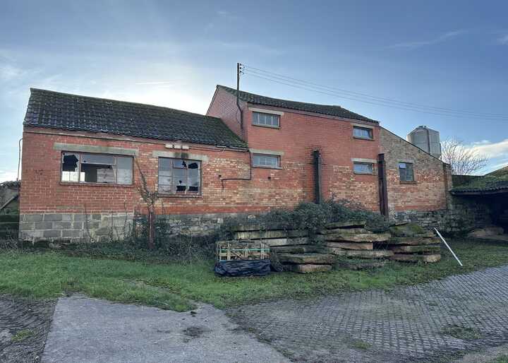A rustic brick building with windows, set against a clear sky and grassy area.